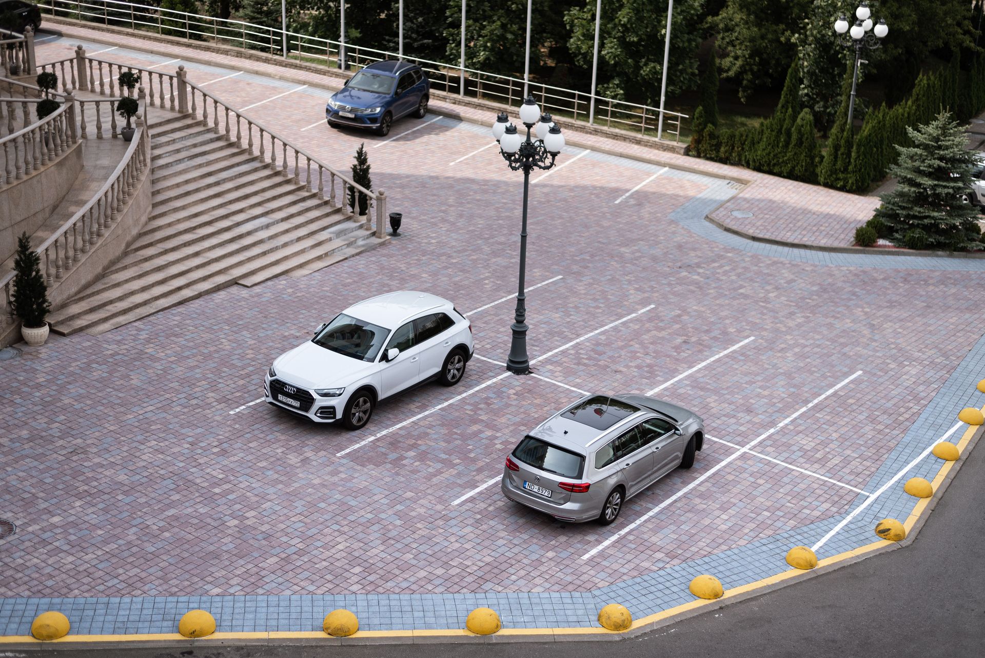 Two cars parked in an elegant outdoor parking lot with surrounding trees.