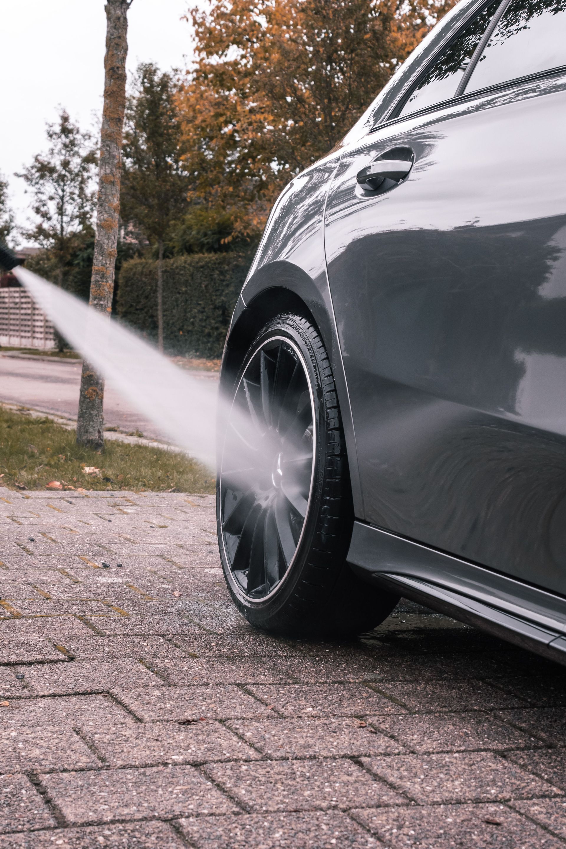 Close-up of a car wheel being cleaned with a high-pressure water stream on a sidewalk.